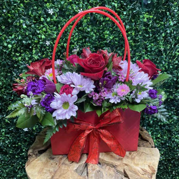Red and purple flower arrangement in a red gift bag with ribbon
