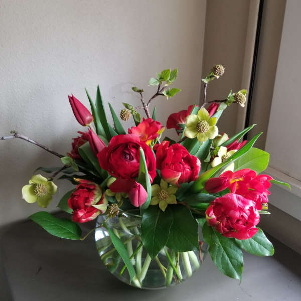 Low round arrangement of red ranunculus and tulips with pale yellow blooms in a clear glass bowl vase.