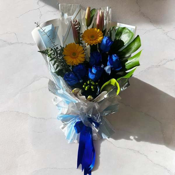 Bouquet of blue roses and yellow gerbera daisies wrapped in pale blue paper