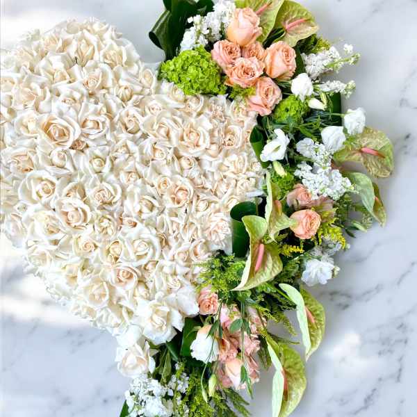 Heart-shaped floral arrangement of white and peach roses with green accents