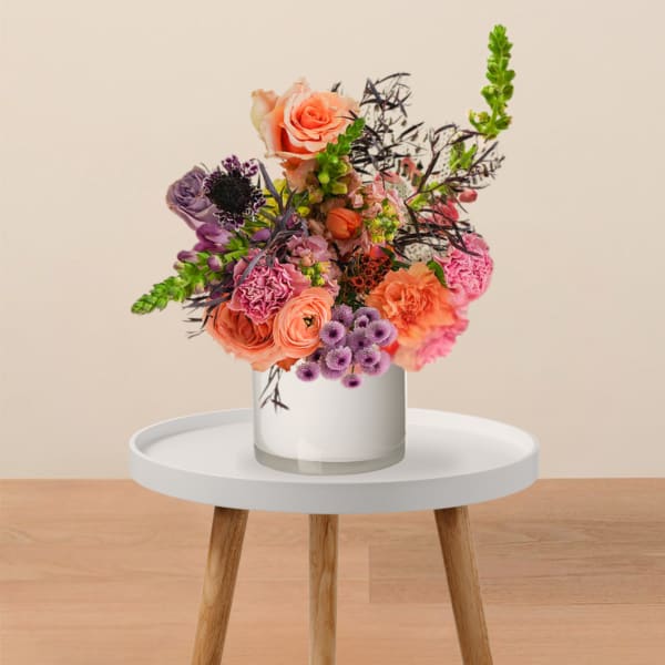 Colorful mixed flower arrangement in a white vase on a small table