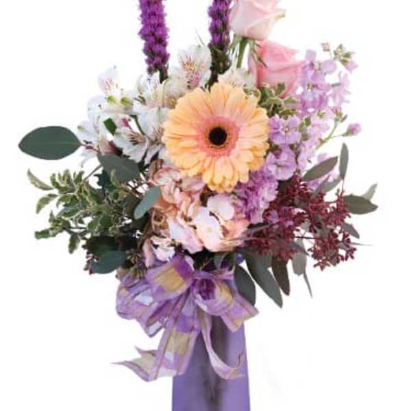 Mixed bouquet with a peach gerbera daisy and pink roses in a purple vase