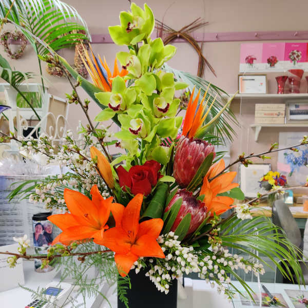 Tropical flower arrangement with orchids, lilies, and protea in a black vase