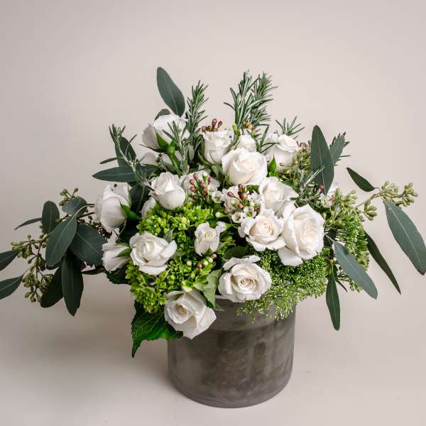 White roses in a gray vase with eucalyptus and green filler flowers