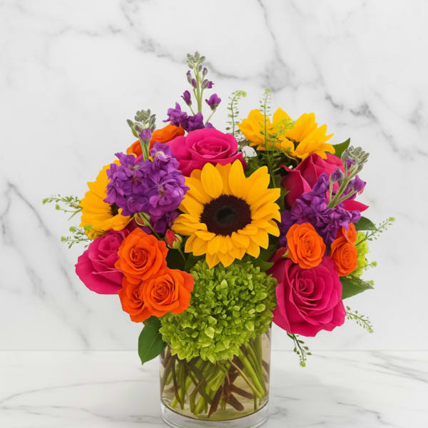 Bright mixed bouquet with roses, sunflowers, and purple blooms in a glass vase