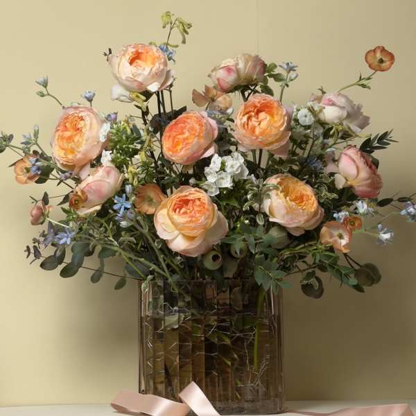 Peach roses and blue accent flowers in a clear glass vase