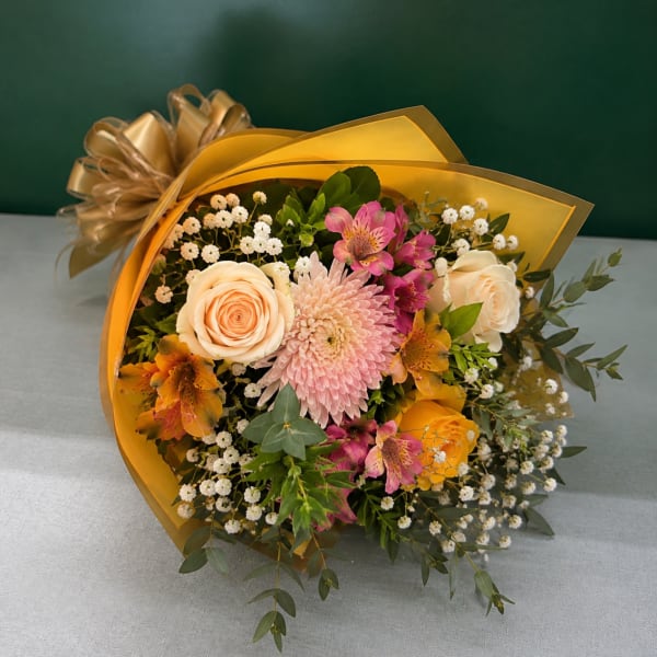 Bouquet of peach and pink flowers wrapped in gold paper