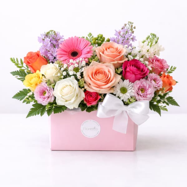 Mixed bouquet of roses and daisies in a pink gift box with a white bow
