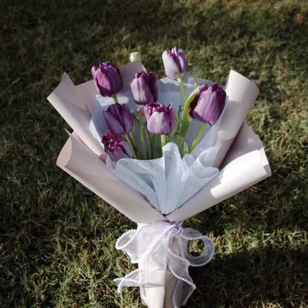 Bouquet of purple tulips wrapped in pale paper with a white ribbon