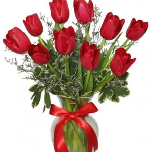 Red tulips arranged in a glass vase with a red ribbon