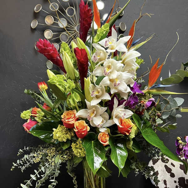 Tall mixed bouquet with white orchids, orange roses, and red tropical blooms in a glass vase