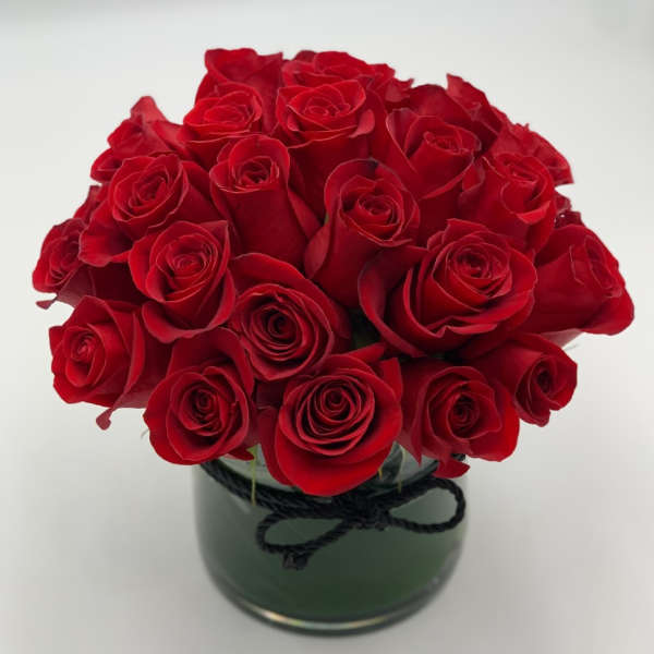 Red roses arranged in a round glass vase with a black ribbon