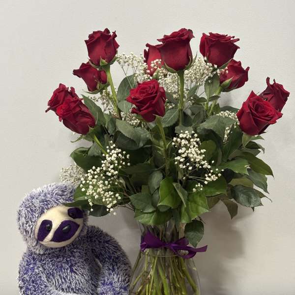Bouquet of red roses in a glass vase beside a purple stuffed sloth
