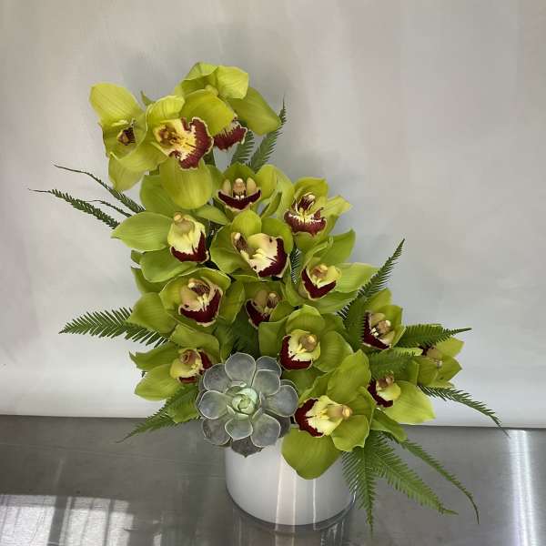Green orchids arranged in a white vase with a small succulent accent