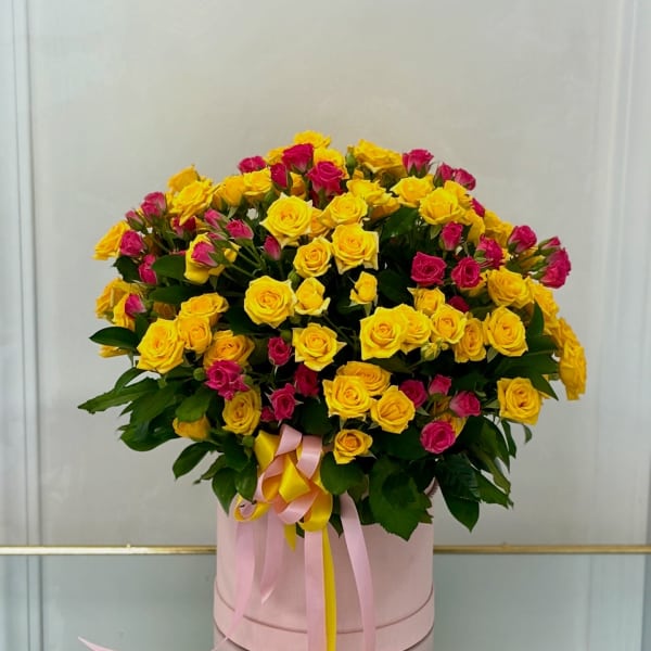 Bouquet of yellow and pink roses in a pink hat box with ribbons