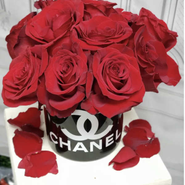 Red roses arranged in a black Chanel box with scattered petals