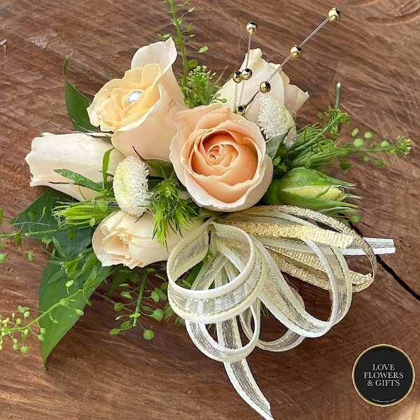 Peach rose corsage with white accents, gold ribbon bow, and jeweled pins on a wooden surface.