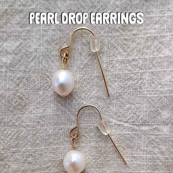 Pair of pearl drop earrings on a textured fabric background