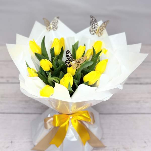 Yellow tulip bouquet wrapped in white paper with a gold ribbon