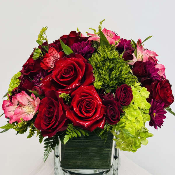 Bouquet of red roses, pink alstroemeria, and purple blooms in a square glass vase