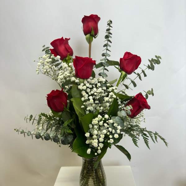 Red roses arranged in a clear glass vase with white filler flowers