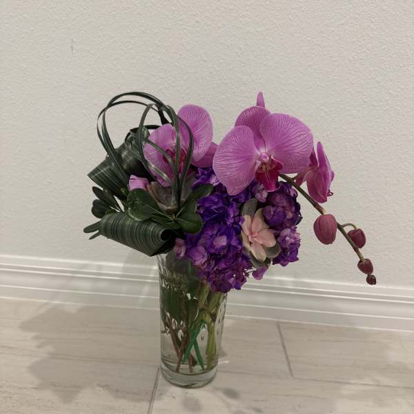 Purple orchids and hydrangeas arranged in a clear glass vase