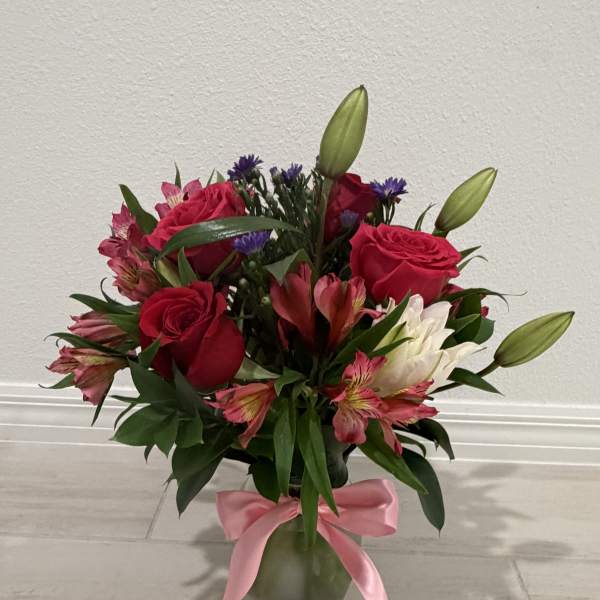 Bouquet of red roses, lilies, and pink flowers in a glass vase with a pink ribbon