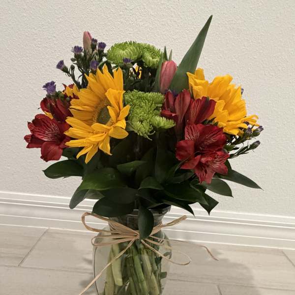 Mixed bouquet of sunflowers, red alstroemeria, and green chrysanthemums in a glass vase