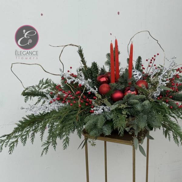 Holiday centerpiece with red candles, ornaments, and evergreen branches