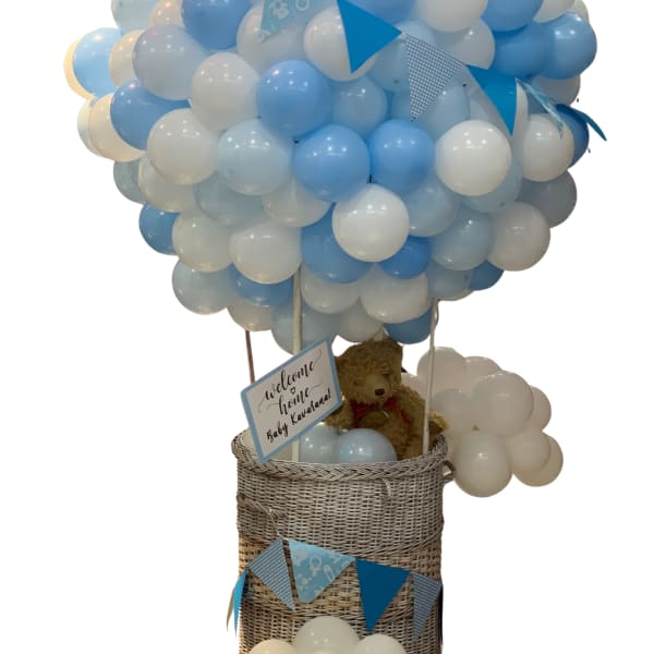 Blue and white balloon arrangement in a wicker basket with a teddy bear