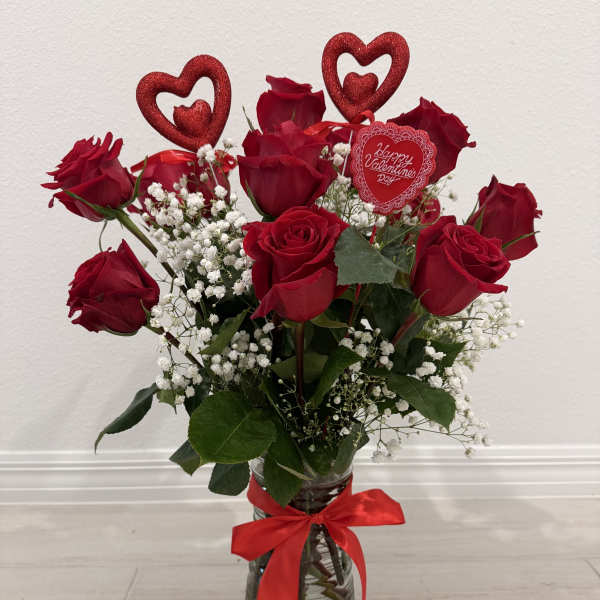 Red roses in a glass vase with baby's breath and a red ribbon