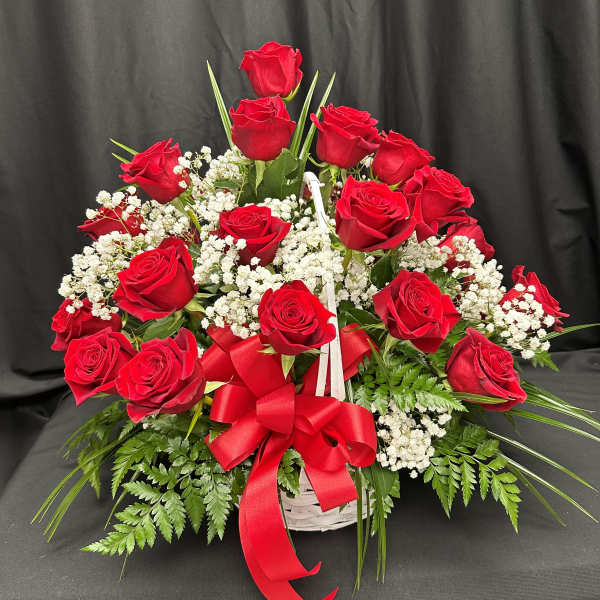 Red roses arranged in a white basket with baby's breath and a red ribbon