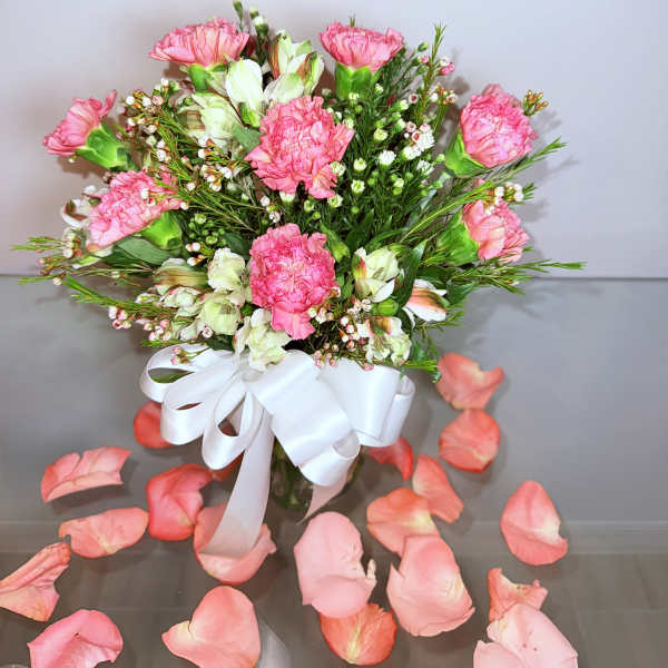 Pink carnations and white blooms in a vase with a white ribbon