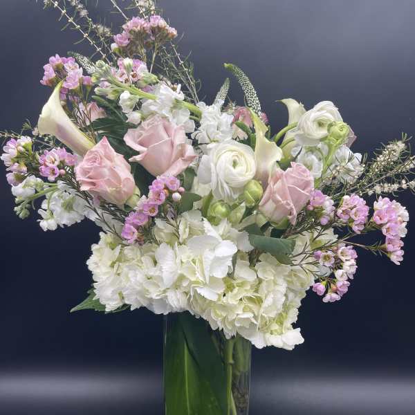 Tall vase arrangement with white hydrangeas, pink roses, calla lilies, and mixed white and pink blooms