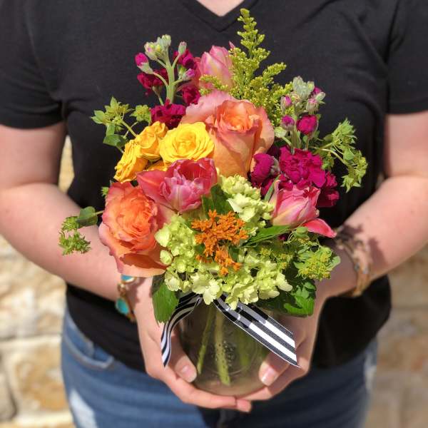 Colorful mixed bouquet of roses and other blooms in a glass vase with ribbon