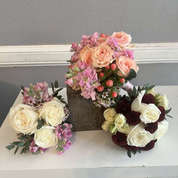Three floral bouquets with roses and pink blooms arranged on a white surface