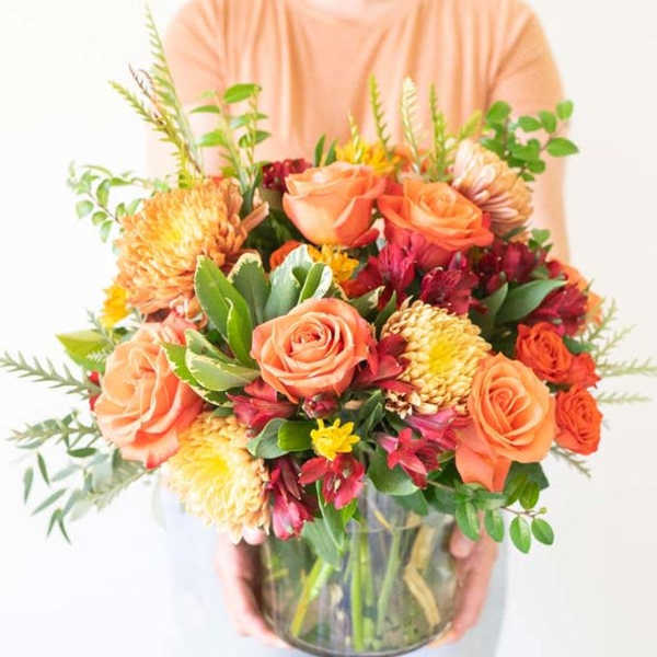 Mixed bouquet of peach roses and orange blooms in a glass vase