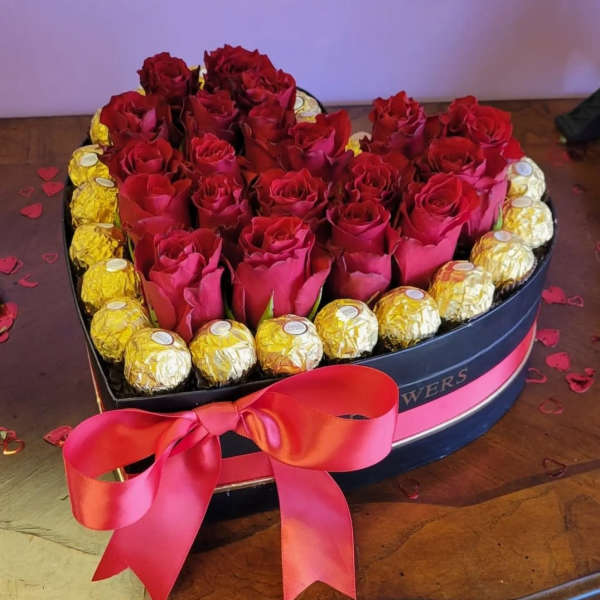 Heart-shaped box of red roses with gold-wrapped chocolates and a pink ribbon