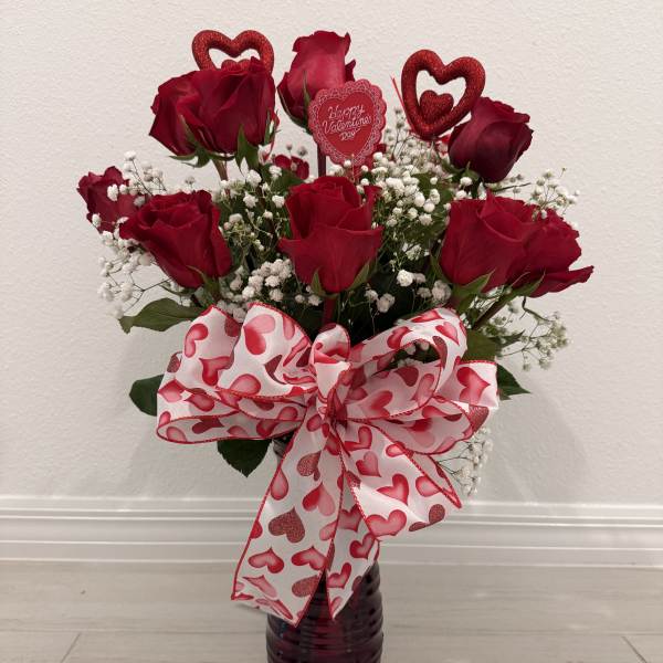 Red roses in a dark vase with a heart-patterned bow and Valentine topper