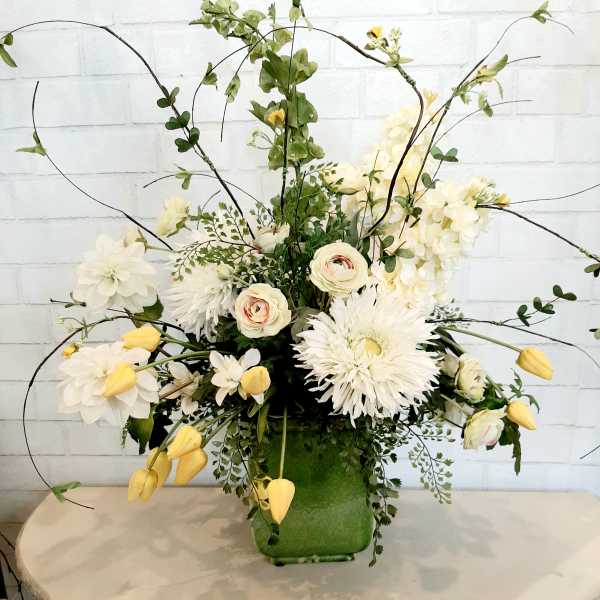 White and pale yellow floral arrangement in a green vase