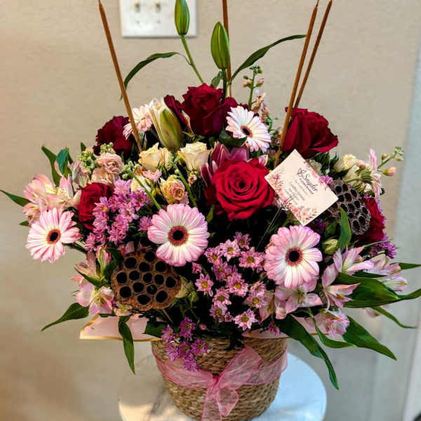 Mixed pink and red flower arrangement in a woven basket with a ribbon