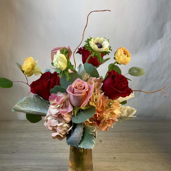 Mixed bouquet of roses, hydrangeas, and anemones in a glass vase