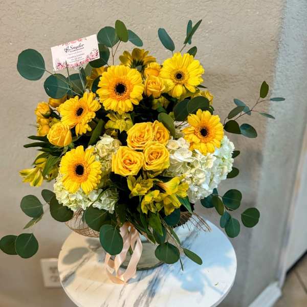 Yellow gerbera daisies and roses in a glass vase with greenery