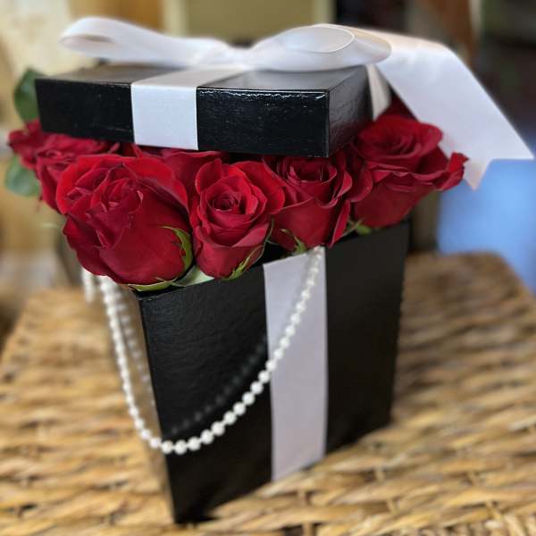 Black gift box filled with red roses and tied with a white ribbon