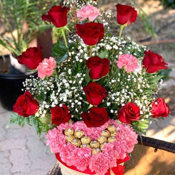Basket arrangement of red roses, pink carnations, and chocolates