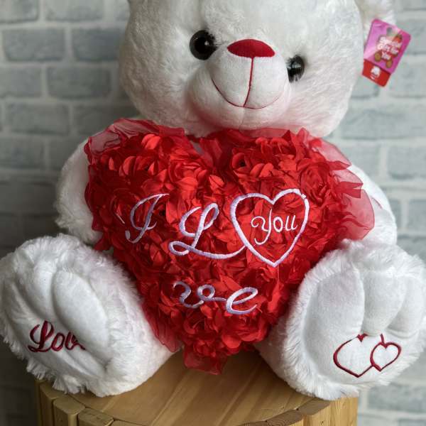 White teddy bear holding a red heart with embroidered love text