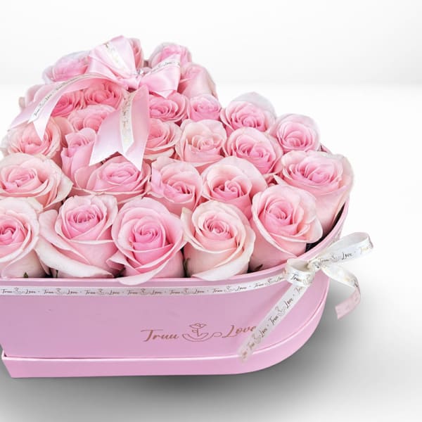 Pink roses arranged in a pink heart-shaped box with ribbon bows