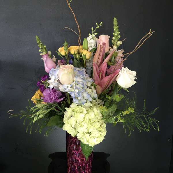 Tall mixed bouquet in a purple vase with roses, hydrangeas, and lilies