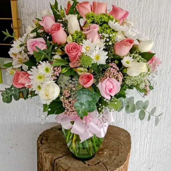Pink and white rose bouquet in a glass vase with a ribbon