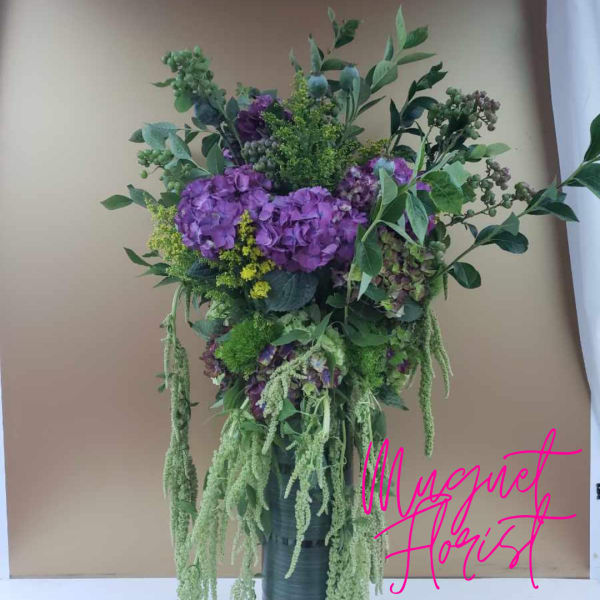 Tall bouquet of purple hydrangeas and mixed greenery in a dark vase